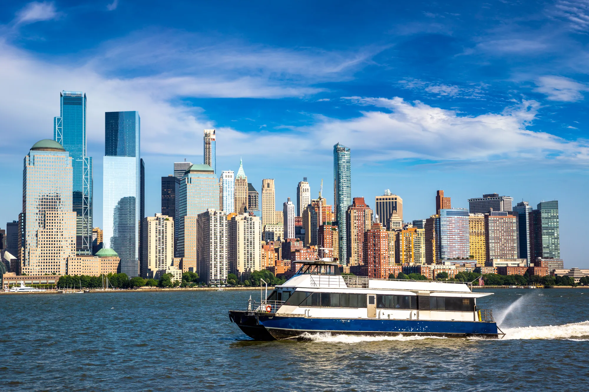 The Rockaway Ferry sails in front of the Manhattan skyline on a sunny day