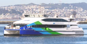 The MV Cetus ferryboat sails through the water. It has a blue, green and white paint job and the San Francisco Bay Ferry logo adorns the side and front of the vessel.