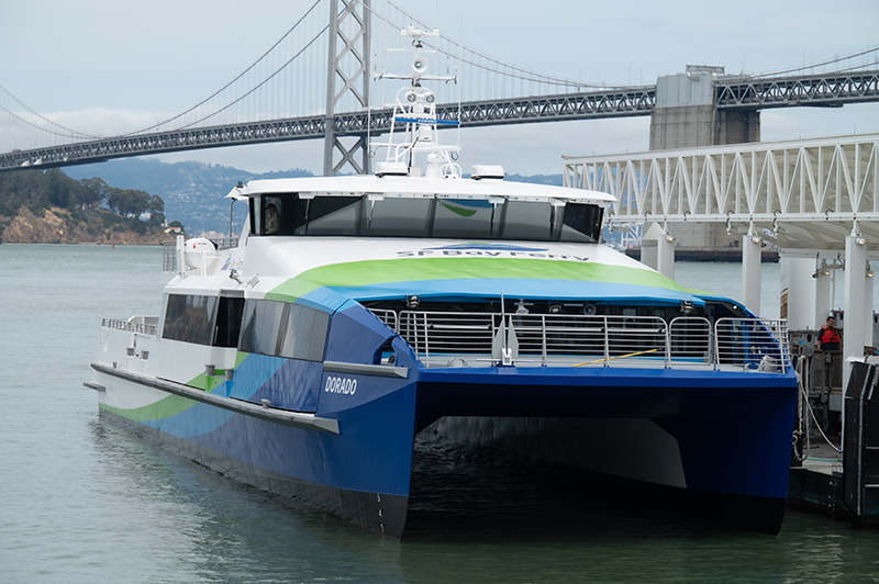 A picture of the MV Dorado docked at the San Francisco Ferry Building during its christening. The Bay Bridge is in the background.